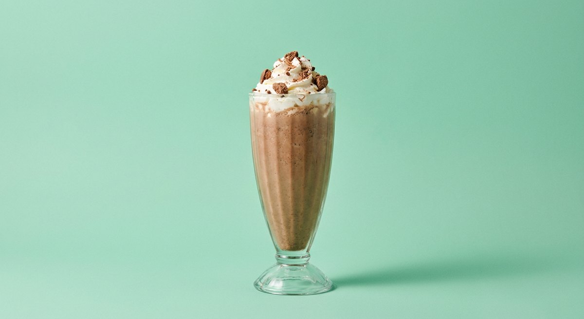 Milkshake de Ovomaltine em copo de vidro, fotografia frontal com fundo colorido